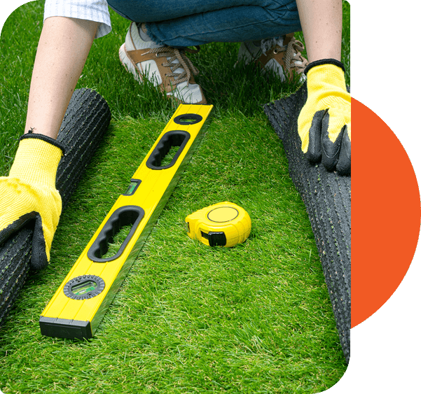 A woman is using a measuring tape to measure the grass for athletic flooring installation.